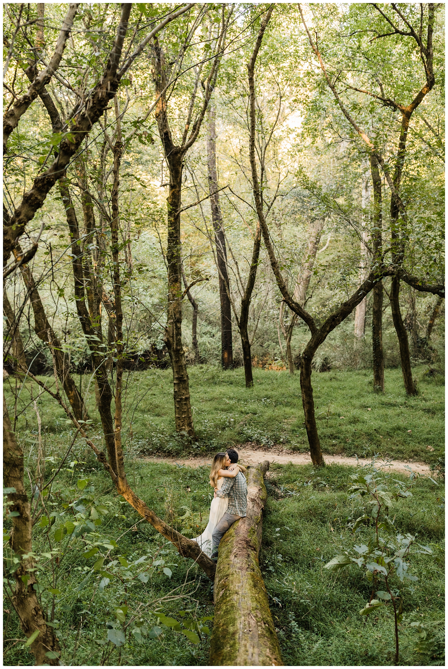 Newly engaged couple in Lullwater Park hugging on a log during an engagement session in a lush, green forest in Atlanta, GA