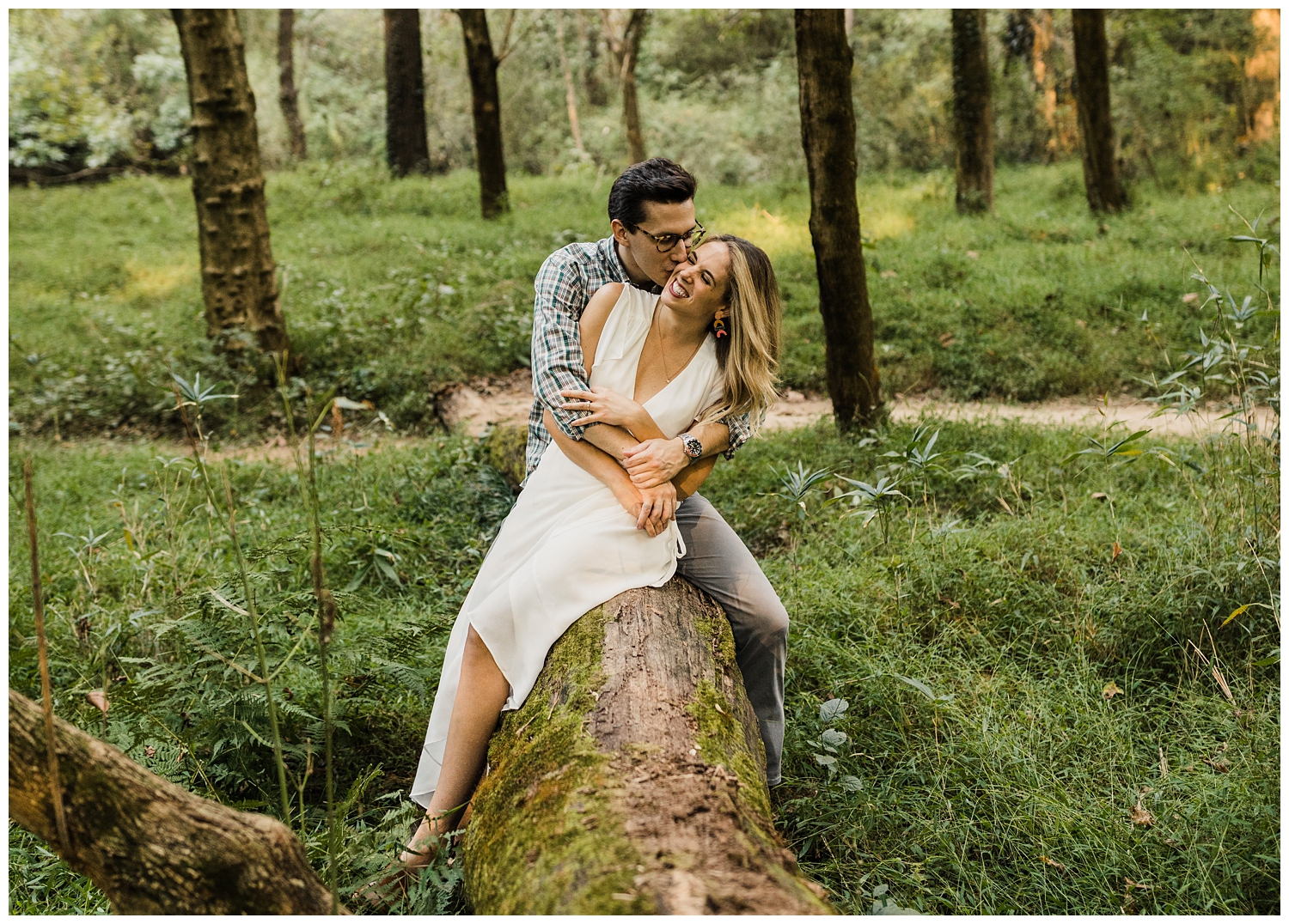 Lullwater Park couple kissing and giggling on a log during an engagement session in a lush, green forest in Atlanta, GA