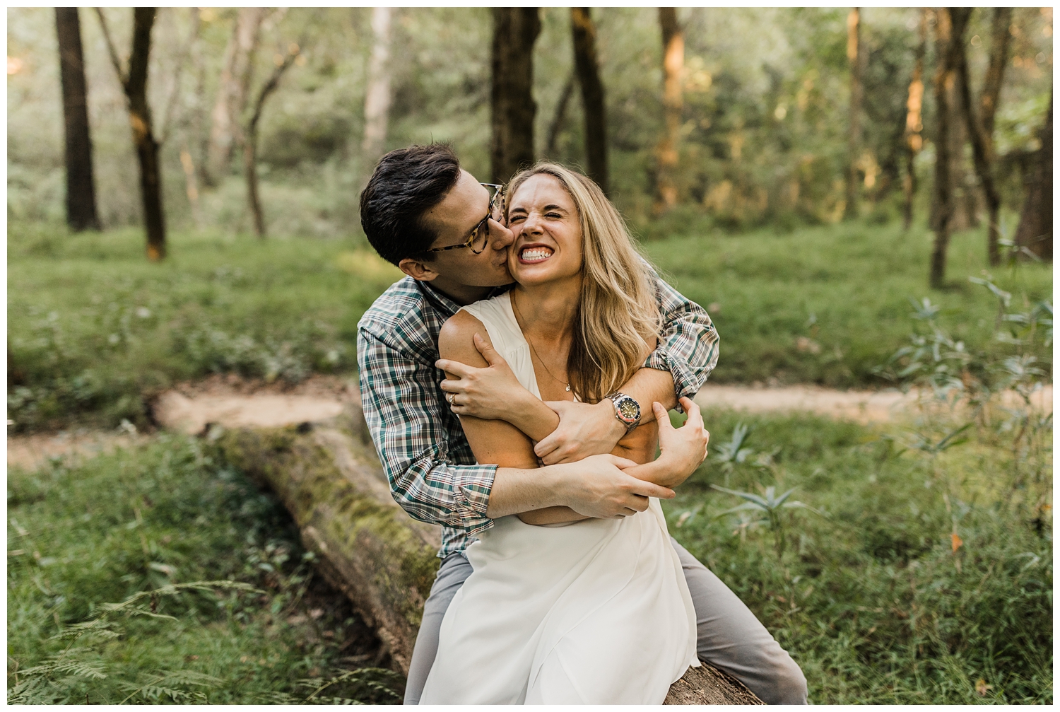 couple laughing on a log during an engagement session in a lush, green forest in Atlanta, GA