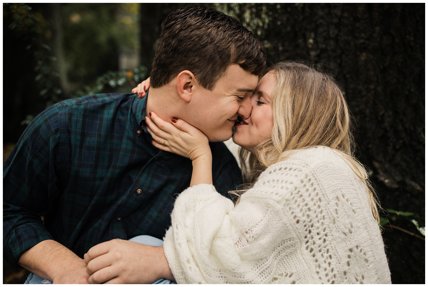rainy day engagement session in marietta, georgia with cute couple sitting and kissing under a tree